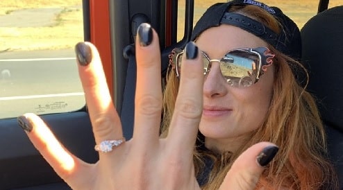 Becky Lynch showing her gold round cut diamond engagement ring. 