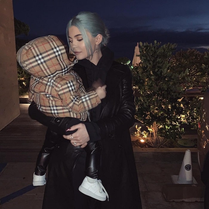 Kylie carrying her baby in a leather coat.