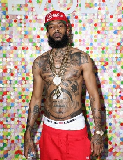 Nipsey Hussle standing while showing his 40 tattoos all over his body.