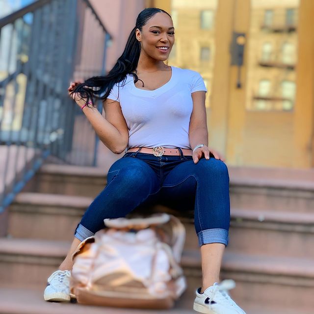 Montana Fishburne sitting on stairs wearing white V neck tshirt and blue jeans