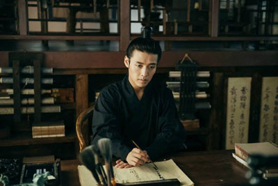 Kang Ha Neul in the library writing down something in his black Korean Traditional dress