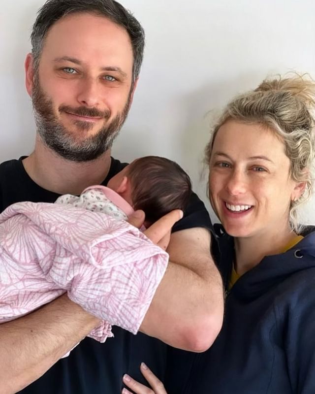Noah Galuten with his family holding his newborn baby girl on a casual dress