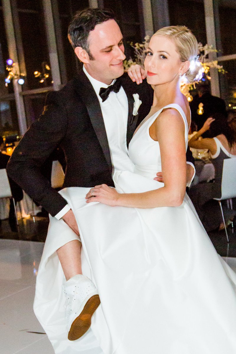 Noah Galuten with his wife Iliza Shlesinger on their wedding day where Iliza is wearing a shoes and a white wedding dress 