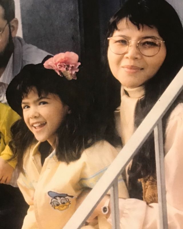 Lilan Bowden picture with her mother when she was a little girl wearing a black hat yellow jacket and a pink flower in her head 