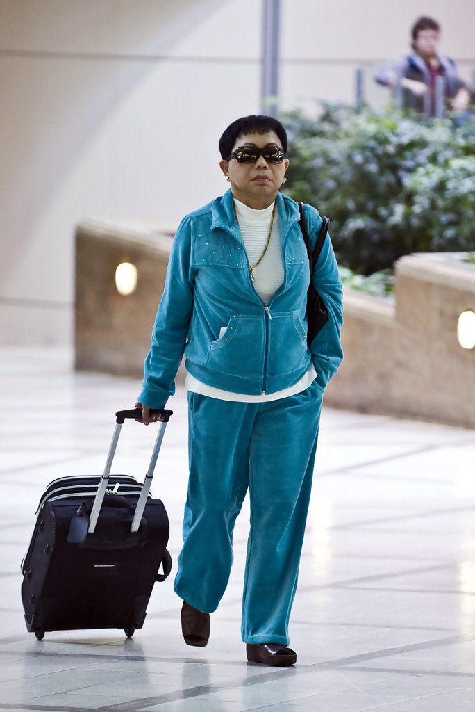 Kultida Woods wearing blue outfit with. black glasses and carring black suitcase with her