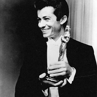 Picture of George Chakiris posing for a photo smiling and looking at another camera holding The Academy Awards