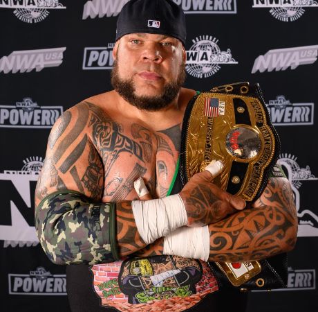 Tyrus posing for a photo shoot while holding a championship belt. 