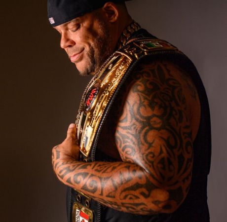 Tyrus posing for a photo shoot while holding a championship belt. 